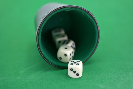 Cubes with dots spill out of a cup onto a vibrant green felt surface, signaling a moment of excitement and anticipation during a friendly game night at home with friends.の写真素材