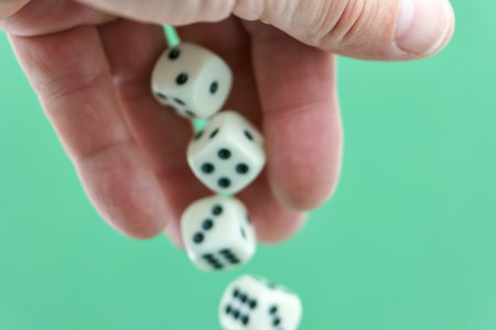 A hand is releasing four dice onto a vibrant green surface, capturing the excitement of a game night. The dice are white with black dots, adding to the playful atmosphere.の写真素材