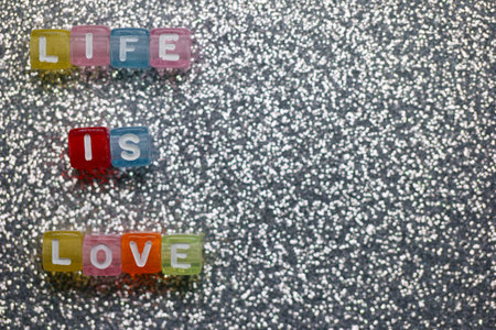 Colorful letter blocks arranged on a glittery surface convey positive messages about life and love,...