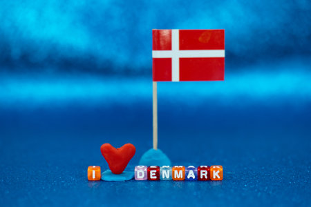 A small Danish flag stands next to a heart shape made of red material, accompanied by colorful letters spelling I DENMARK on a bright blue surface, showcasing national pride.の写真素材