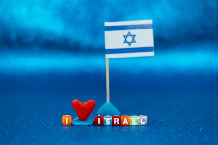 A red heart made of modeling clay and a small flag symbolize affection for Israel. Colorful letters spell out the word Israel, set against a vibrant blue background.の写真素材