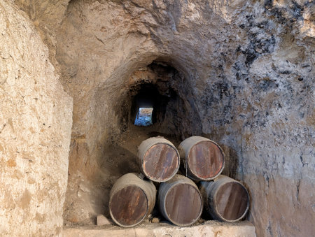 Within an ancient underground tunnel, several barrels are stacked against a rough stone wall.の写真素材