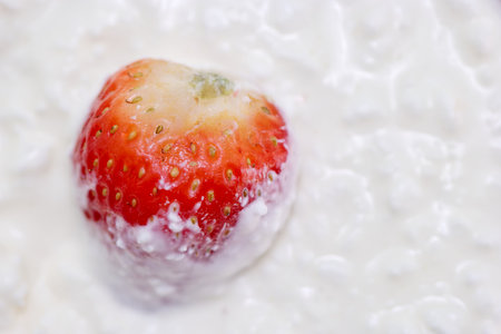 A vibrant strawberry floats in a rich, creamy background, with the texture of the cream surrounding it creating a visually appealing contrast. The scene highlights freshness and indulgence.の写真素材