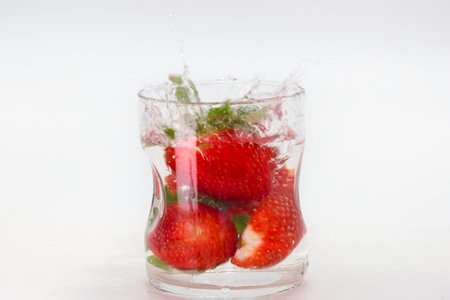 Strawberries drop into a glass of water, producing splashes and bubbles while showing freshness and vibrancy on a warm summer day. The scene captures a moment of enjoyment and relaxation.の写真素材