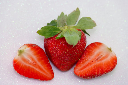 A vibrant red strawberry sits between two halves of the fruit, showing its juicy interior and green leaves against a sparkling background, highlighting freshness.の写真素材