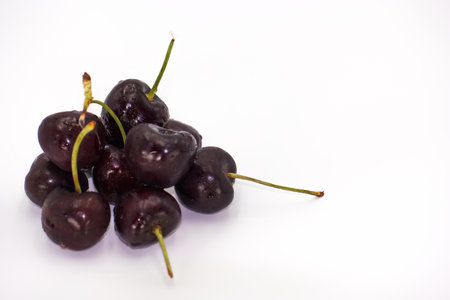 Juicy black cherries are stacked neatly, showing their shiny skin and green stems against a plain white background. Perfectly ripe and ready to eat.の写真素材