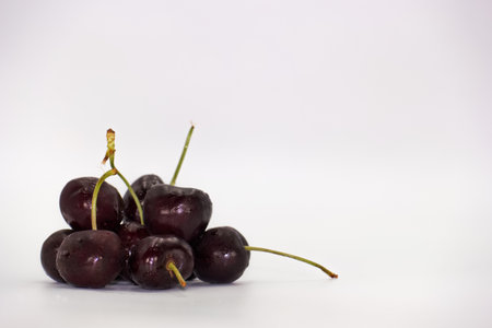 Dark red cherries clustered together on a smooth white surface, highlighting their glossy skin and slender stems, creating an appealing still life composition.の写真素材