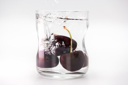 Fresh cherries drop into a glass filled with clear water, causing a dynamic splash. Bubbles rise to the surface, and the vibrant fruit contrasts beautifully with the liquid.の写真素材