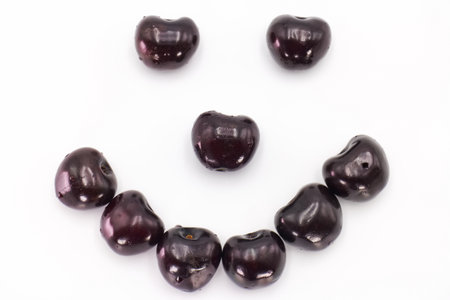 Black beans are arranged creatively to form a smiley face design. The glossy surface reflects light, enhancing the playful appearance against a crisp white backdrop.の写真素材