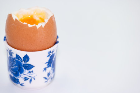 A soft boiled egg with a slightly cracked shell is placed in a blue floral patterned egg cup. The...