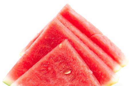 Several vibrant watermelon slices are arranged neatly in a pyramid shape on a plain white background, emphasizing their juicy red flesh and fresh green rind, ideal for summer enjoyment.の写真素材
