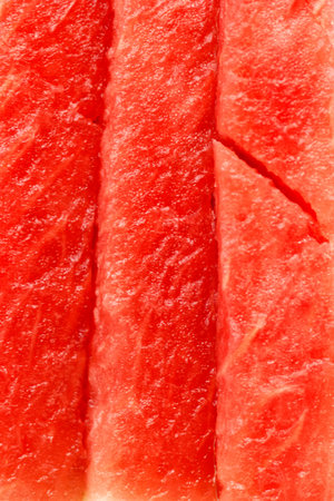 Brightly colored watermelon slices are neatly arranged on a wooden surface, showing the juicy pink flesh and refreshing appeal of summer fruit. Natural light enhances the vibrant colors.の写真素材
