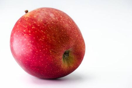 A bright red apple rests on a plain white surface, highlighting its glossy skin and natural shine. The apple features a small brown spot, adding to its organic appearance.の写真素材