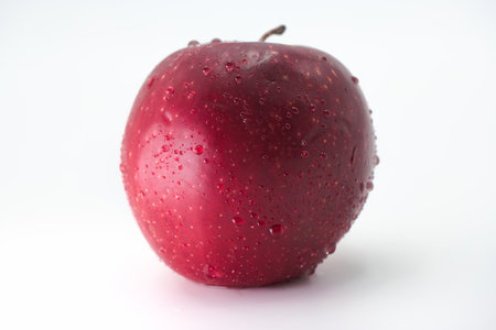 A vibrant red apple is covered in tiny water droplets, showing its freshness and shine. The background is plain white, emphasizing the apple's rich color and texture.の写真素材