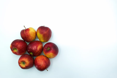 A cluster of red apples is arranged neatly on a clean white surface, showing their vibrant colors and natural shine in bright daylight, inviting healthy snacking.の写真素材