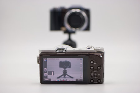 A digital camera is mounted on a tripod, displaying its settings on the screen. In the background, another camera is also visible, creating a creative photographic setup.の写真素材