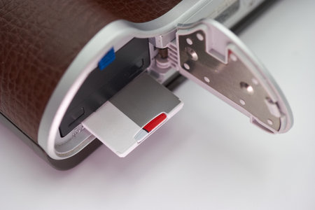 A camera is displayed with its compartment open, showing a silver memory card with a red section. The texture of the camera body is visible, enhancing the detailed view of the technology.の写真素材
