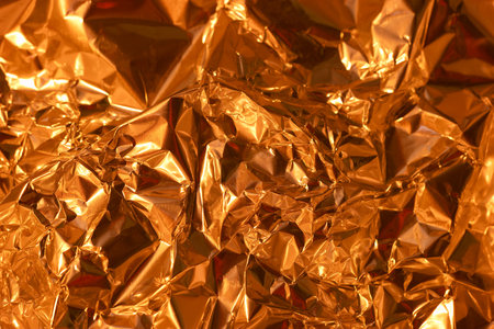 The surface displays a vibrant golden hue with numerous folds and crinkles that create an eye catching texture. Light glimmers off the metallic surface, enhancing its visual appeal.の写真素材
