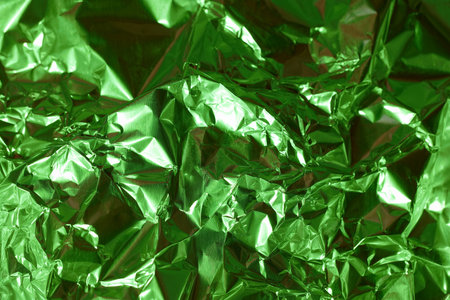 Crumpled green foil displays a shiny surface, reflecting light in various directions. The patterns intricately create a vibrant and textured visual appeal, suitable for creative backgrounds.の写真素材