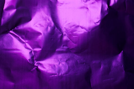 Crumpled purple foil fills the setting, showing a rich texture and deep hue. Soft light enhances the folds and shadows, adding depth to the vibrant color.の写真素材