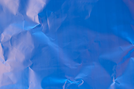 Soft curves and creases create a dynamic interplay of light and shadow on crumpled blue paper, capturing an artistic essence that intrigues the viewer's eye.の写真素材