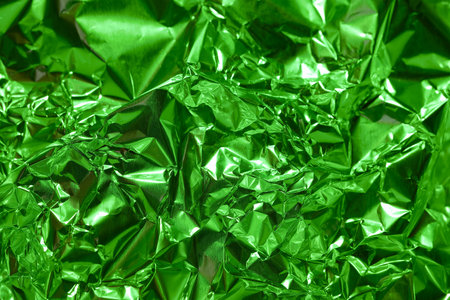 Vivid green metallic foil is tightly crumpled, showcasing a dynamic texture that reflects light in multiple directions. Ideal for crafts or artistic backgrounds.の写真素材