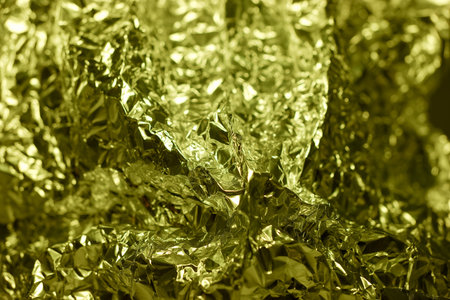 A crumpled sheet of golden foil is illuminated brightly, showing its shiny, reflective texture and intricate folds.の写真素材