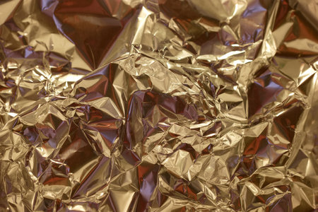 The surface features crinkled golden foil that reflects light, creating a dynamic interplay of shadows and highlights. The intricate textures add depth and interest to the surface.の写真素材