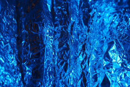 Shimmering blue metallic foil displays a textured surface with folds and reflections under soft light. The vibrant color enhances the overall visual appeal and depth.の写真素材