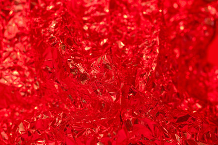 A textured surface of crumpled red foil catches light, creating a captivating abstract background. The shiny, reflective material offers a unique visual quality suitable for various applications.の写真素材