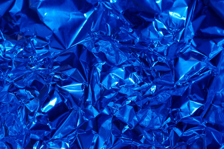 Shimmering crinkled blue foil showcases vibrant textures and reflections, ideal for creative projects, backgrounds, or artistic photography. Its unique surface enhances visual appeal.の写真素材