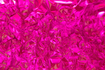 Shiny pink foil is crumpled and reflective, creating dynamic patterns as light interacts with its surface. The vibrant color enhances the textured appearance, making it visually striking.の写真素材