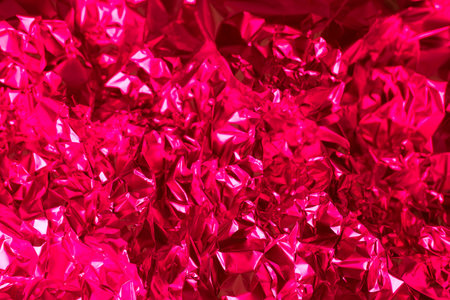 Crumpled, shiny red foil fills the frame, showcasing a playful, textured surface that reflects light. This vibrant material exudes energy and could enhance various artistic projects or celebrations.の写真素材