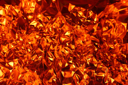 Crumpled orange foil glimmers with rich, warm tones, showcasing intricately textures that inspire artistic expression and modern design in various projects.の写真素材