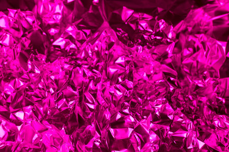 Shiny crumpled foil in vibrant pink fills the frame, showing intricate folds and reflections of light, creating a rich and dynamic visual texture suitable for various artistic applications.の写真素材