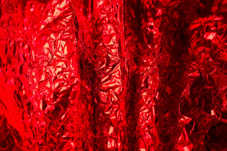 The bright crumpled red foil displays an array of shiny textures, catching light dramatically. This vivid backdrop enhances creativity and visual appeal for various artistic projects.の写真素材