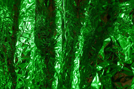 A close up view reveals crinkled green metallic foil, reflecting light and creating vibrant textures. The intricate folds and reflective surfaces add depth and intrigue to the composition.の写真素材