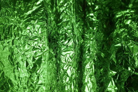 Shimmering green foil reflects light and creates a dynamic texture, showing different folds and creases that enhance visual interest in a bright setting.の写真素材