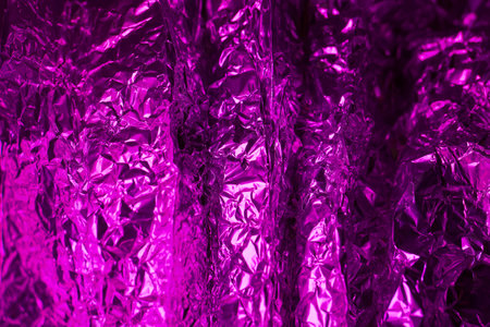 Shimmering purple foil reveals a complex interplay of light and shadows, highlighting the crinkled surface and adding depth to the vibrant color scheme.の写真素材
