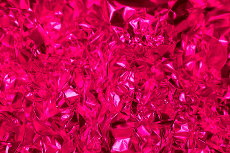 A bright pink foil surface is crumpled and textured, reflecting light in various directions. This dynamic background brings energy and creativity to artistic endeavors, enhancing visual appeal.の写真素材