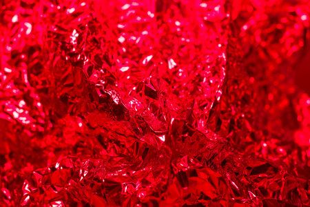 A close up view of crumpled red foil showcases a vibrant array of textures and reflections. The light creates a shimmering effect, enhancing the vivid color and details.の写真素材