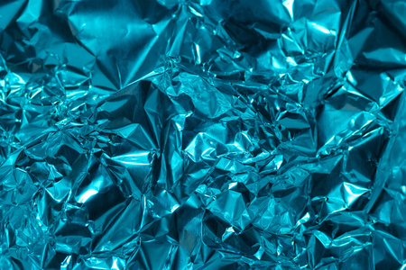 Crumpled blue foil reflects natural light, creating a vibrant texture. The shiny surface displays various patterns and depths, emphasizing its metallic quality.の写真素材