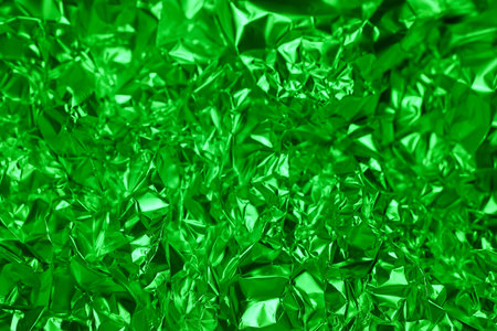 Crumpled green foil displays a shiny, textured surface that gleams under direct light. The intricate folds and reflections create an eye catching visual effect, enhancing its vibrant color.の写真素材