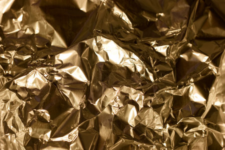 Wrinkled golden foil displays an array of textures and reflections, creating an eye catching backdrop perfect for artistic projects or decorative purposes. The interplay of light enhances its allure.の写真素材