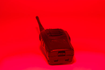 A communication device rests on a flat surface, illuminated by a vibrant red light. The dark environment enhances the device's features, creating an engaging visual.の写真素材