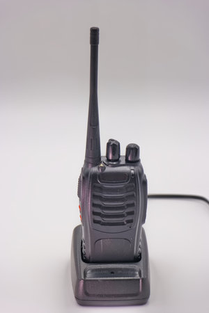 A walkie talkie is resting on its charging dock, showing its sleek design and antenna. The background is minimalistic, emphasizing the device's functionality and features.の写真素材