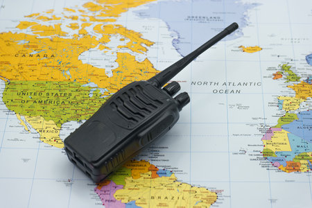 A black communication device is placed on a detailed world map that shows various countries and oceans, illustrating global connectivity. The map features vibrant colors and diverse geography.の写真素材