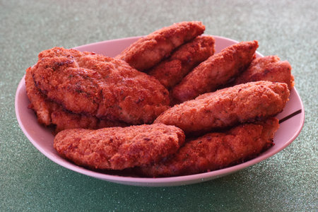 A delicious assortment of crispy fried chicken tenders sits on a white platter. Perfectly cooked and...