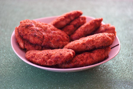 A plate filled with crispy fried chicken pieces is displayed on a bright green surface, perfect for...
