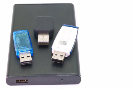 A portable hard drive sits on a clean surface with three USB flash drives on top. Each flash drive...